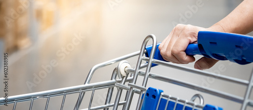 Customer hand holding shopping cart in grocery store or supermarket aisle.