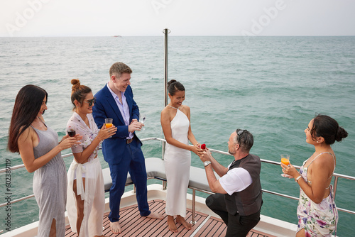 elderly man showing engagement ring and surprise his girlfriend and friends joined in congratulations or success in a party on luxury yacht © offsuperphoto