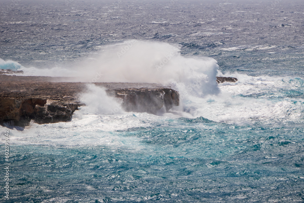 Seascape during a storm. Sea with blue water and big waves, waves hitting the rocks with big splashes