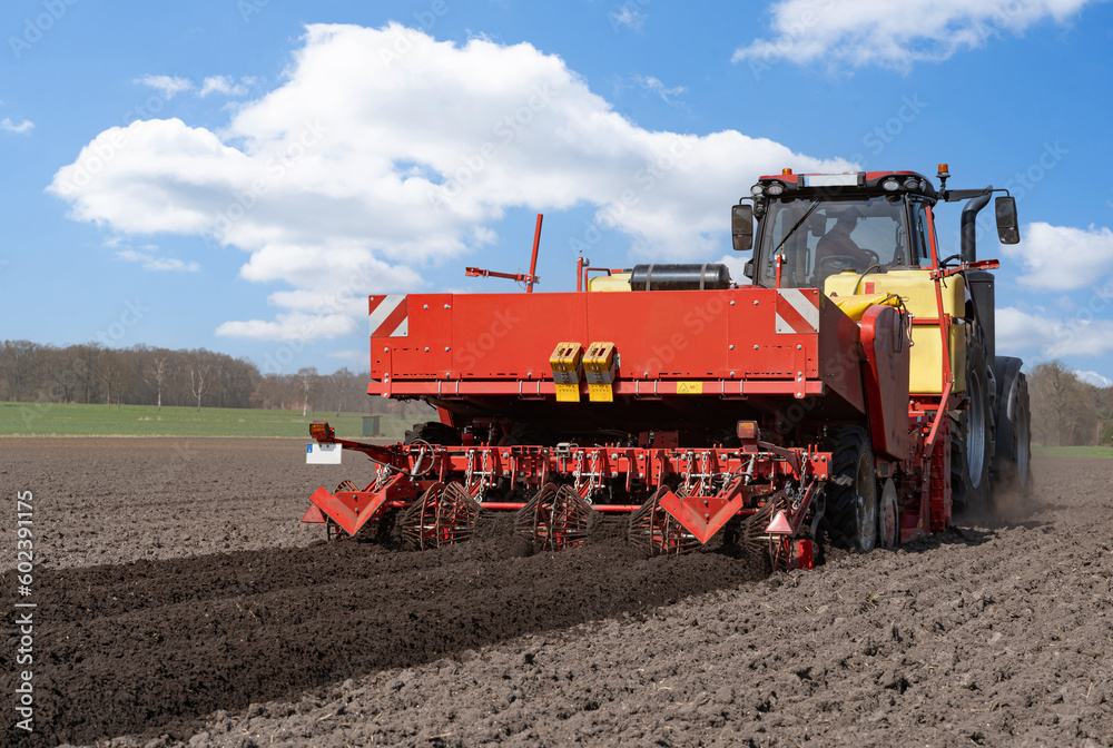 Großer, roter Traktor mit einer Karoffelpflanzmaschine im Frühjahr auf dem Kartoffelfeld im Einsatz. Großer, roter Traktor mit einer Karoffelpflanzmaschine im Frühjahr auf dem Kartoffelfeld im Einsatz.
