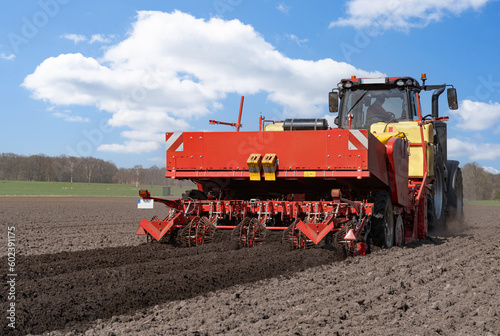 Großer, roter Traktor  mit einer Karoffelpflanzmaschine im Frühjahr auf dem Kartoffelfeld im Einsatz. 