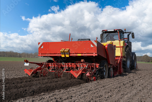 Großer, roter Traktor mit einer Karoffelpflanzmaschine im Frühjahr auf dem Kartoffelfeld im Einsatz. 