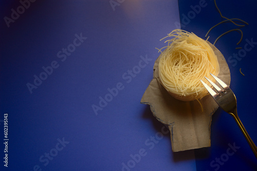 Human head with a nest of spaghetti thoughts and a silver fork. The concept of mental health, exhaustion, chaotic thoughts, psychology of emotion and the study of the human brain