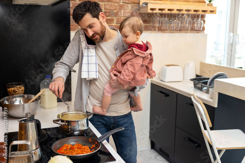 Father looking after baby girl making meal and talking on mobile phone, multitasking man.