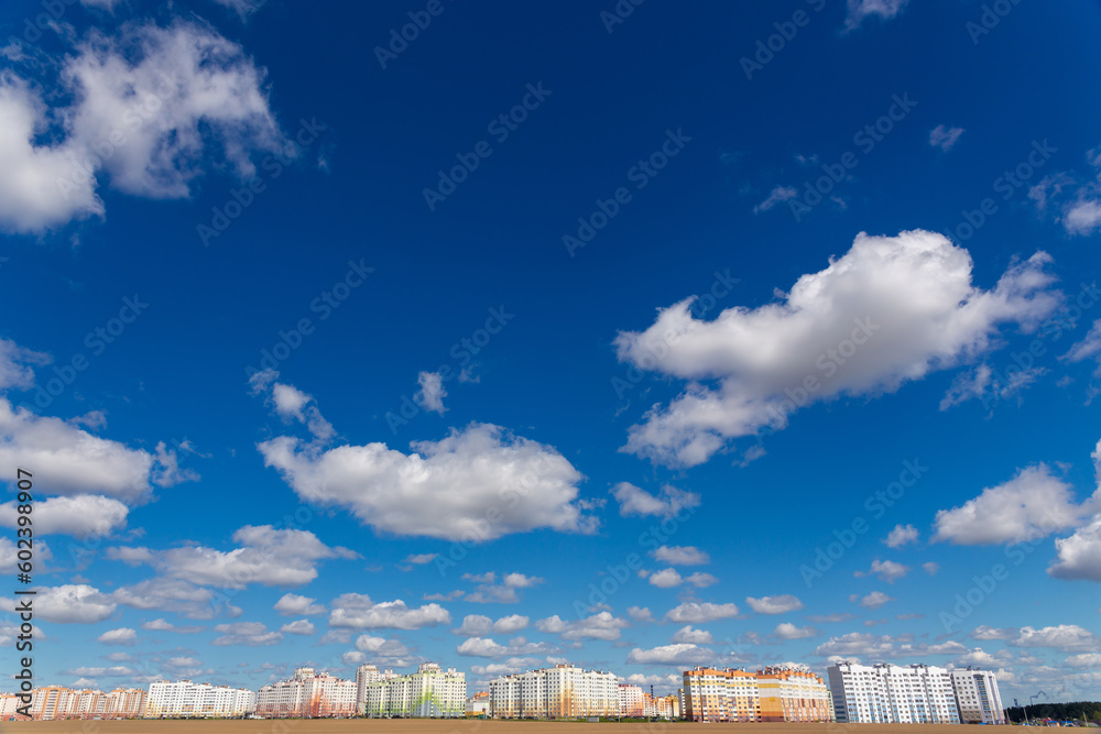 Deep blue skies with white clouds background and modern multi-storey residential area on the horizon