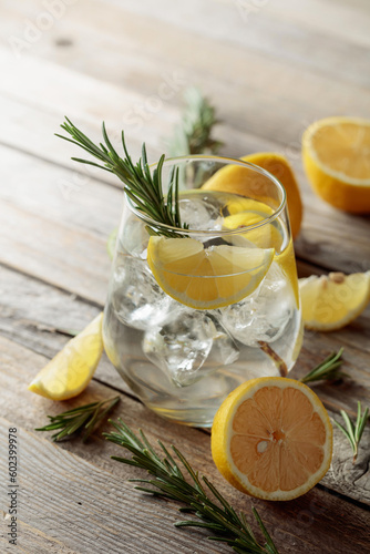 Gin tonic with ice, rosemary, and lemon slices on an old wooden table.