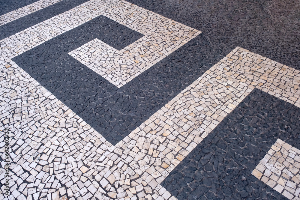 Fototapeta premium Traditional design on cobblestone sidewalk, Funchal, Madeira island, Portugal. Black and white mosaic floor from calcada tiling.