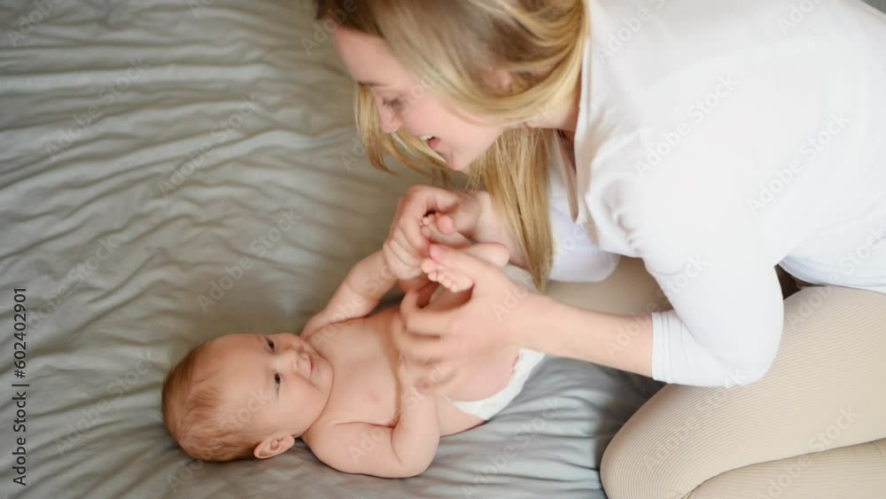 Joyful young mother plays with her baby lying on the bed,smiles,kisses,enjoys motherhood.Concept of family,love and care Joyful young mother plays with her baby lying on the bed,smiles,kisses,enjoys motherhood.Concept of family,love and care