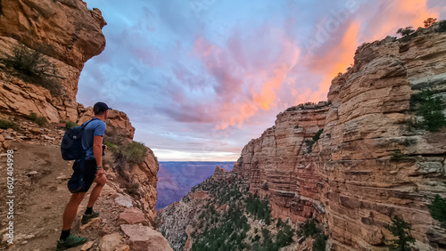 Rear view of man with backpack hiking along Bright Angel trail with panoramic aerial overlook of South Rim of Grand Canyon National Park, Arizona, USA, America. Amazing vista after sunrise in summer