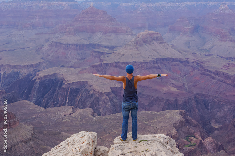 Rear view of man in tank top spreading arms and standing on edge of rock on Bright Angel trail with scenic aerial view of South Rim of Grand Canyon National Park, Arizona, USA, America. Amazing vistas