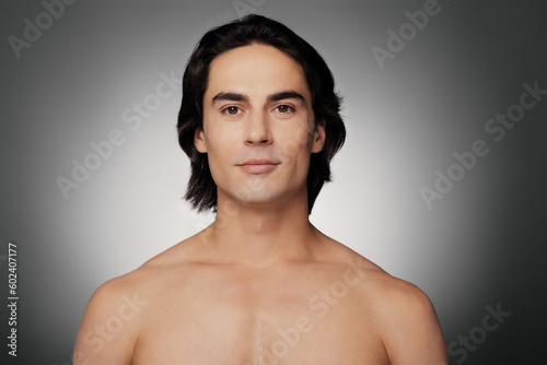 Portrait of young shirtless man looking at camera against grey background