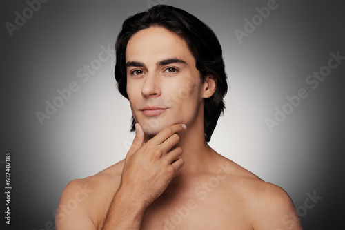 Portrait of shirtless young man holding hand on chin against grey background