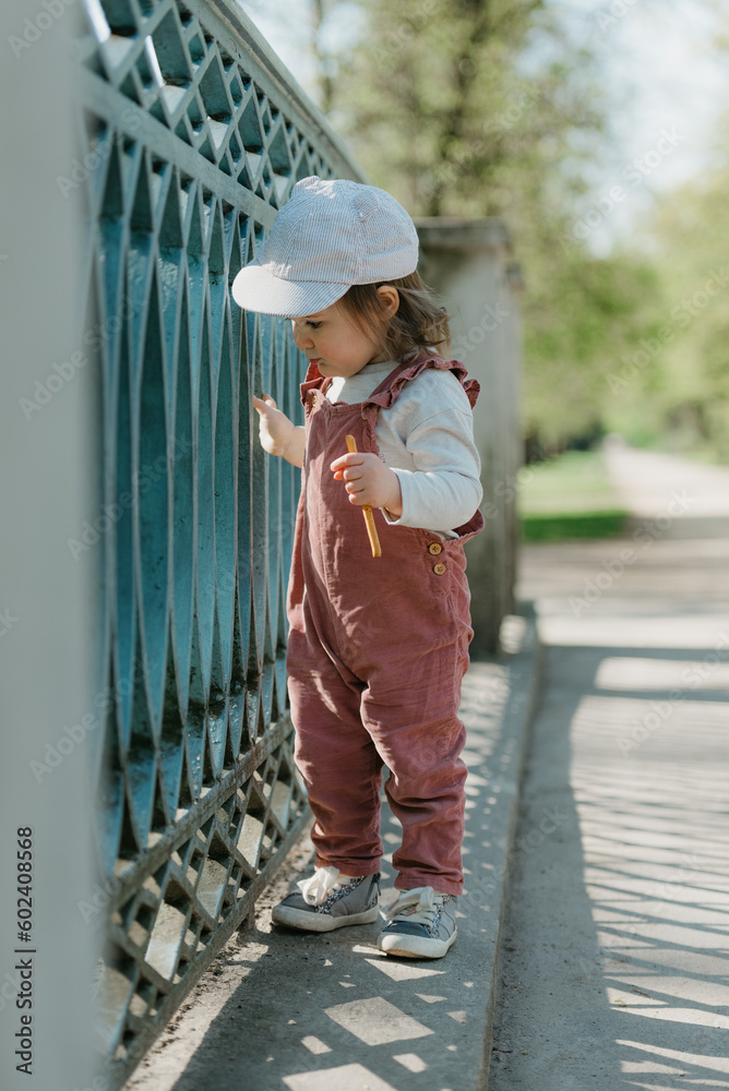 A female toddler walks near the garden bridge fence.