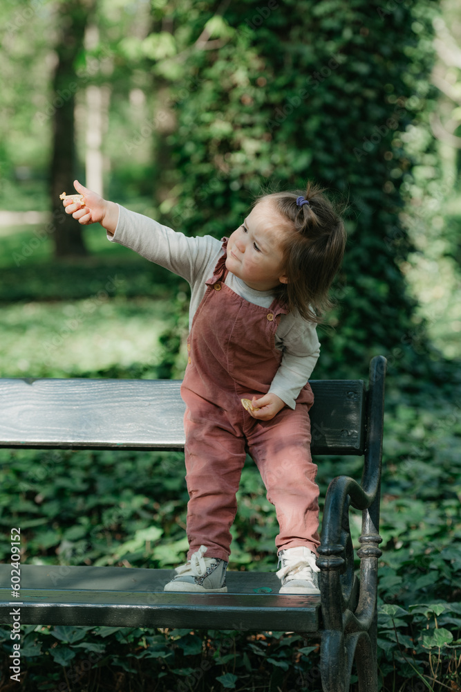 A female toddler is on the garden bench in the park.
