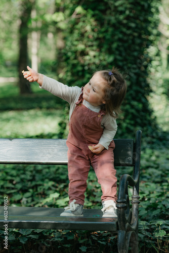 Obraz na płótnie A female toddler is on the garden bench in the park. w salonie