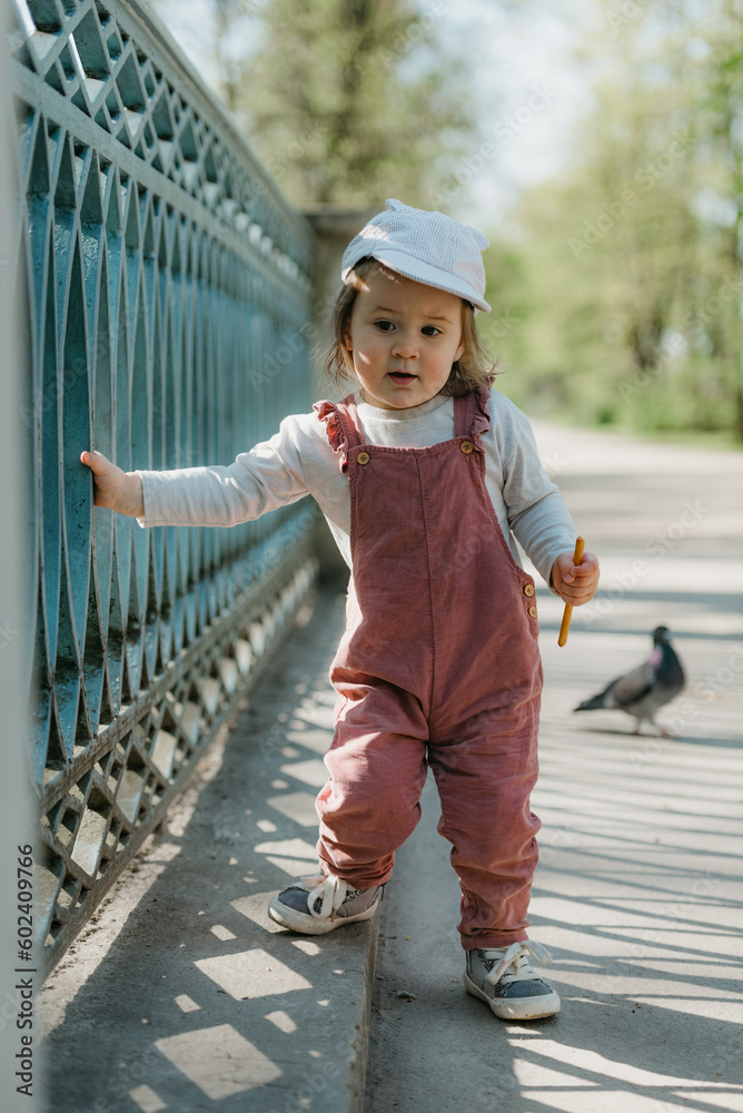 A female toddler walks near the garden bridge fence.