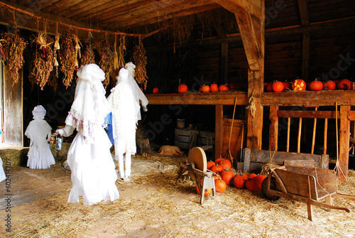 Ghosts are arranged in a historic wooden Colonial barn, surrounded by pumpkins, on Halloween