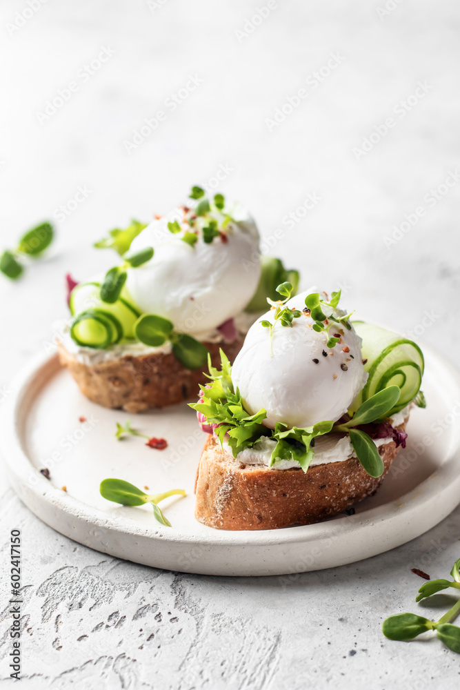 Poached egg sandwiches with cucumber and microgreens. Healty breakfast bruschetta on light background. Keto diet, text space Poached egg sandwiches with cucumber and microgreens. Healty breakfast bruschetta on light background. Keto diet, text space