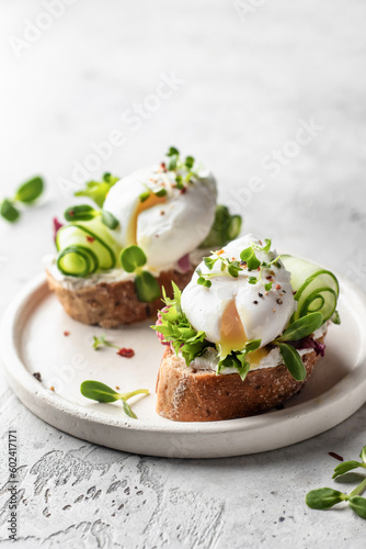 Poached egg sandwich with cucumber and microgreens. Healty breakfast bruschetta on light background. Keto diet, text space
