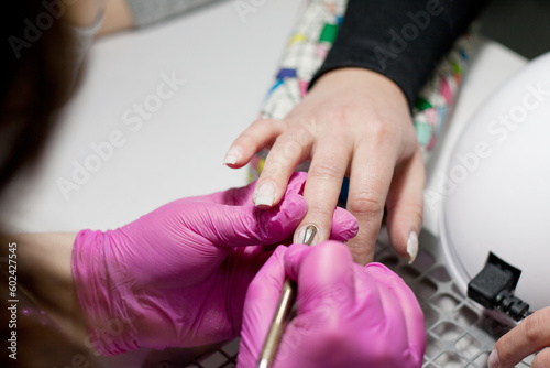 Salon manicure. Professional combined manicure in beauty salon. Manicurist in pink gloves uses special manicure tools. closeup of hands of manicurist and client. Professional hand care.