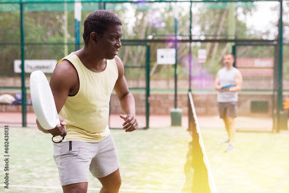 Young adult man playing paddle tennis with partners at warm sunny day, healthy lifestyle concept