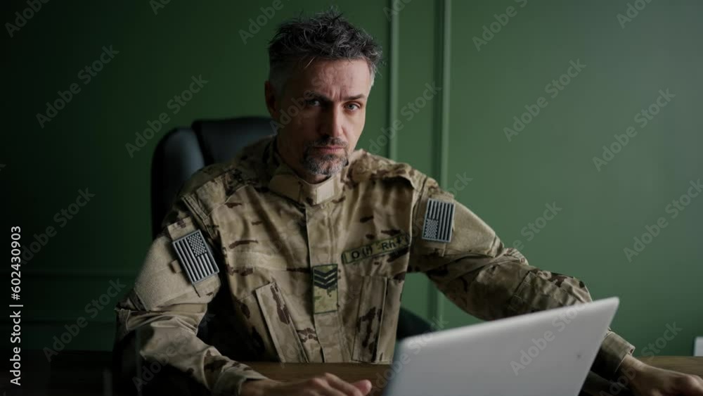 Soldier working with laptop in home. Look at the camera. Everyday life of a military man in reserve. Work and communication online