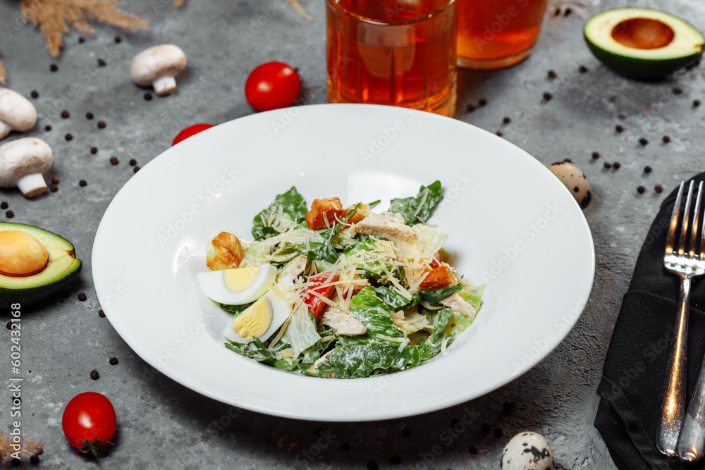 Traditional caesar salad in a white bowl on a old white table with leaves and a sauce boat and parmesan. Selected focus. Traditional caesar salad in a white bowl on a old white table with leaves and a sauce boat and parmesan. Selected focus.