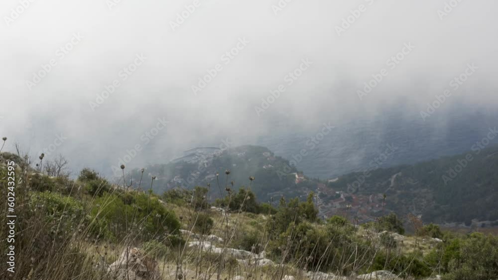 Clouds flow past mountain side looking down at town on coast of Croatia Clouds flow past mountain side looking down at town on coast of Croatia