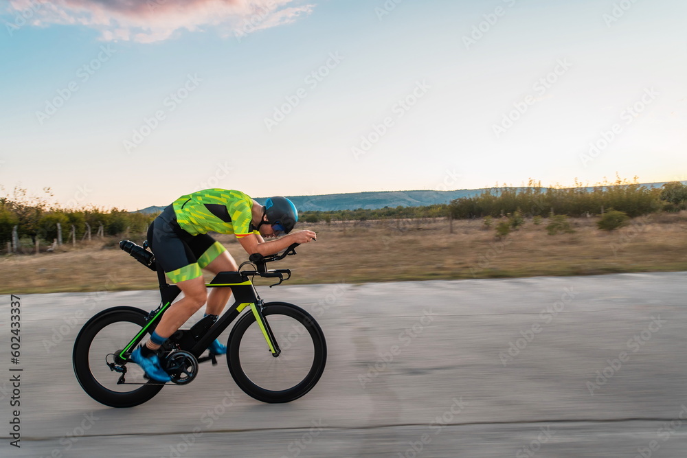Fototapeta premium Triathlete riding his bicycle during sunset, preparing for a marathon. The warm colors of the sky provide a beautiful backdrop for his determined and focused effort.