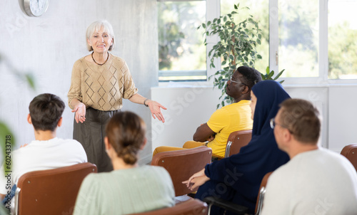 Mature female teacher giving lecture to group of multinational students in classroom