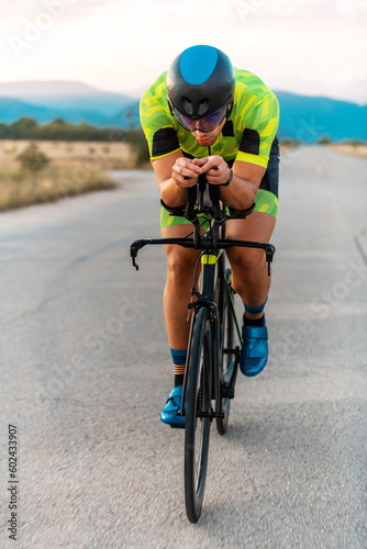  Triathlete riding his bicycle during sunset, preparing for a marathon. The warm colors of the sky provide a beautiful backdrop for his determined and focused effort.