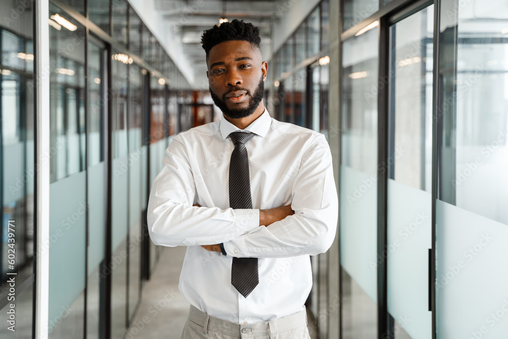 Fototapeta premium Young corporate african american man standing in the office corridor wearing a white shirt and black tie