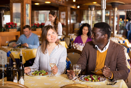 Positive couple  Caucasian woman and African-american man eating in restaurant and talking.