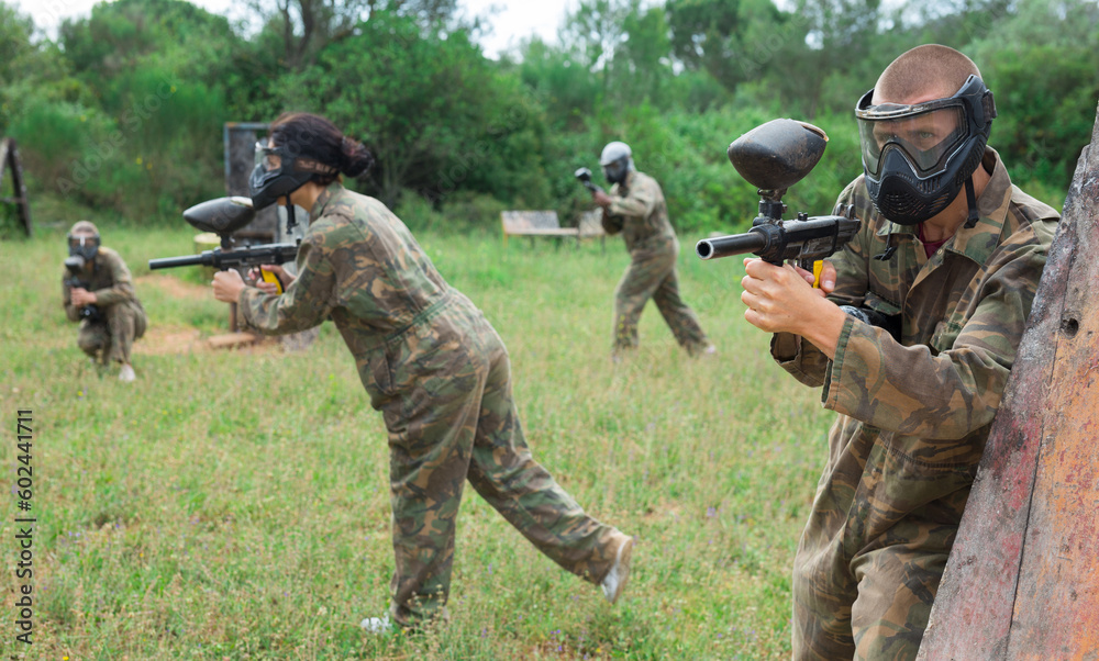 Fototapeta premium Excited male and female paintball players in protective uniform aiming and shooting with guns