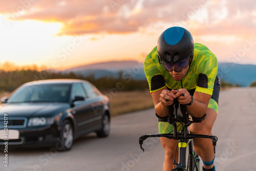  Close up photo of triathlete riding his bicycle during sunset, preparing for a marathon. The warm colors of the sky provide a beautiful backdrop for his determined and focused effort.