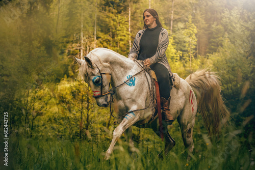 Portrait of a woman on her american native decorated white arabian horse in spring outdoors