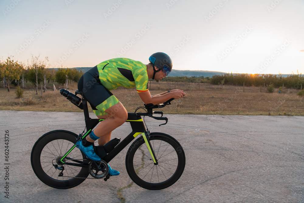 Triathlete riding his bicycle during sunset, preparing for a marathon. The warm colors of the sky provide a beautiful backdrop for his determined and focused effort. Triathlete riding his bicycle during sunset, preparing for a marathon. The warm colors of the sky provide a beautiful backdrop for his determined and focused effort.