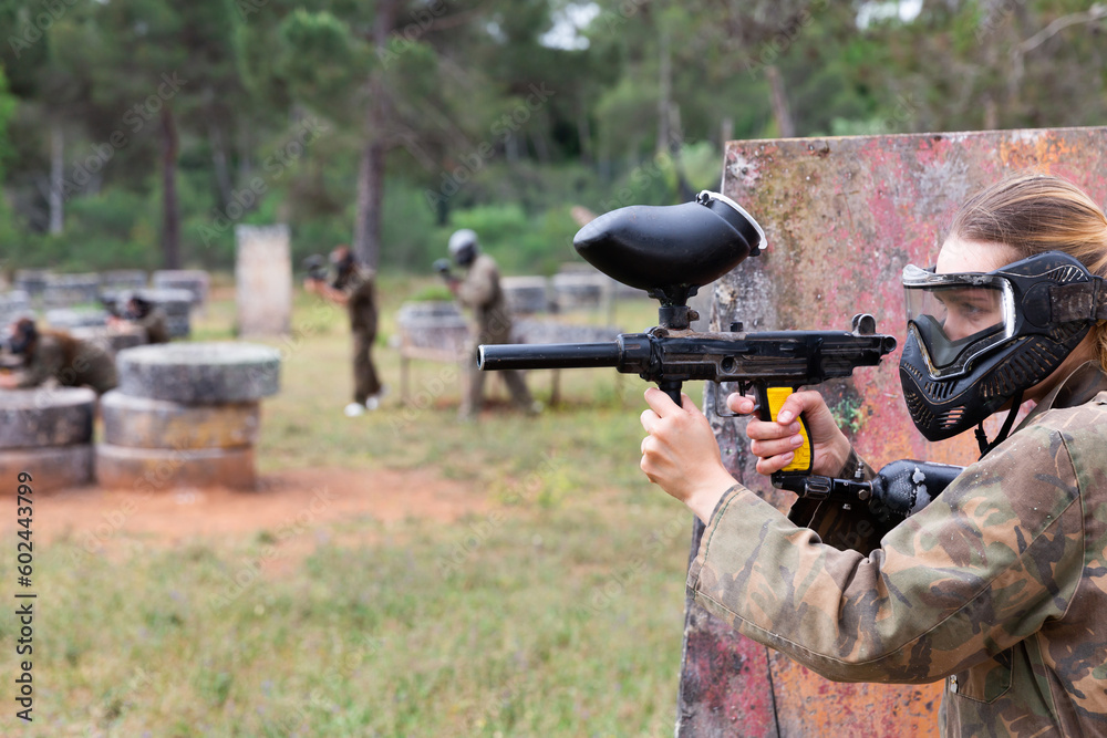Fototapeta premium Paintball players of one team in camouflages and masks aiming with gun in shootout playing field