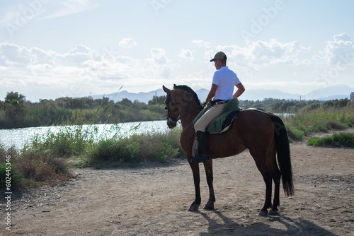 Spanish man in a white shirt riding a horse on the beach. Man with a horse on the beach. A boy riding a galloping mare on the sand. Spanish horse rider enjoying a horseback ride under a clear sky.