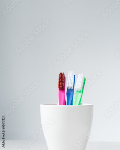 Blue  pink and green toothbrush with white bristles in a cup with a white background  colorful toothbrushes with copyspace