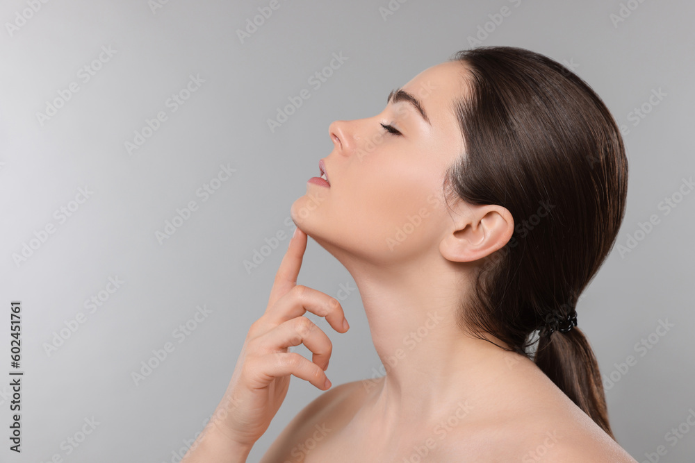 Young woman massaging her face on grey background. Space for text Young woman massaging her face on grey background. Space for text