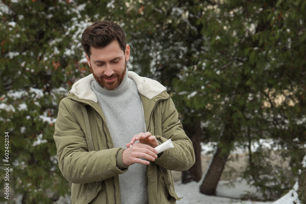 Man applying cream from tube onto hand outdoors, space for text. Winter care Man applying cream from tube onto hand outdoors, space for text. Winter care