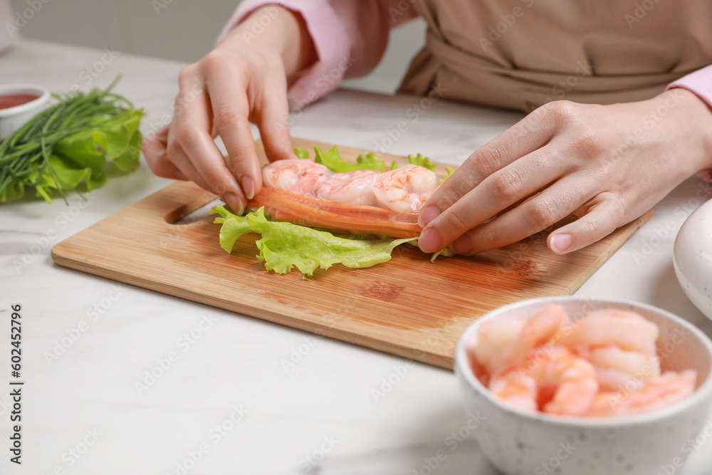 Woman making delicious spring roll at white marble table, closeup