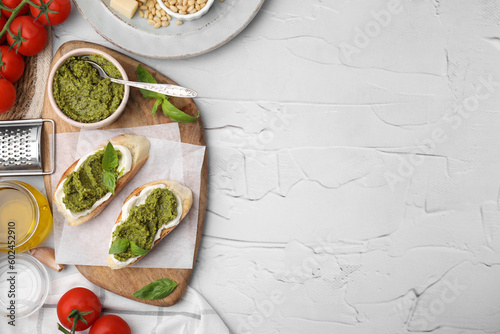 Tasty bruschettas with pesto sauce and ingredients on white textured table, flat lay. Space for text