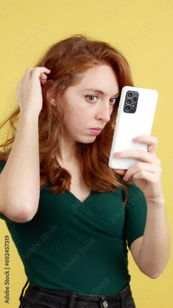 Red-haired woman touching her hair looking reflected in the mobile Red-haired woman touching her hair looking reflected in the mobile