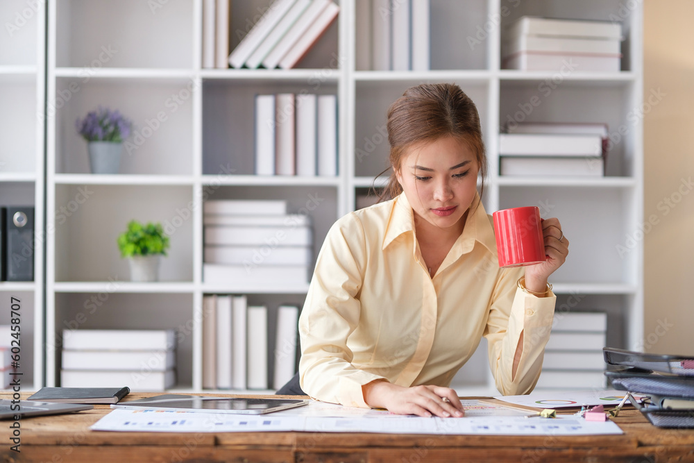 Image of female accountant drinking coffee and reading financial paper report, doing paperwork at desk. Image of female accountant drinking coffee and reading financial paper report, doing paperwork at desk.