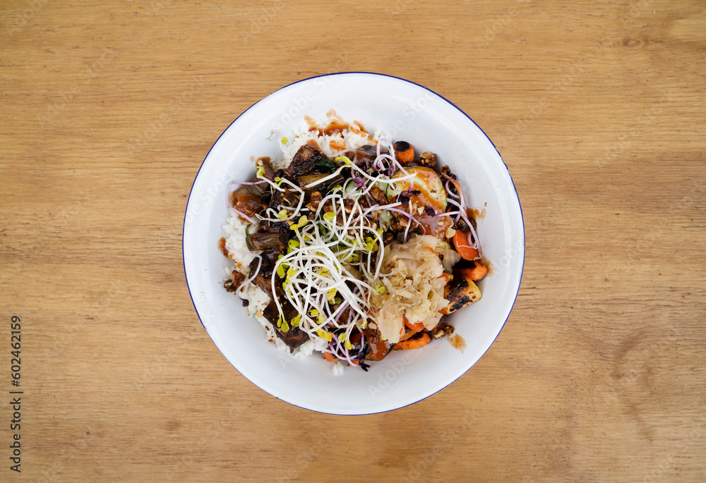 Vegan cuisine. Gluten free. Top view of a bowl with grilled tofu, soy sprouts, pumpkin seeds, season vegetables, spicy mango, sushi rice, cucumber and kimchi, in the restaurant wooden table. Vegan cuisine. Gluten free. Top view of a bowl with grilled tofu, soy sprouts, pumpkin seeds, season vegetables, spicy mango, sushi rice, cucumber and kimchi, in the restaurant wooden table.