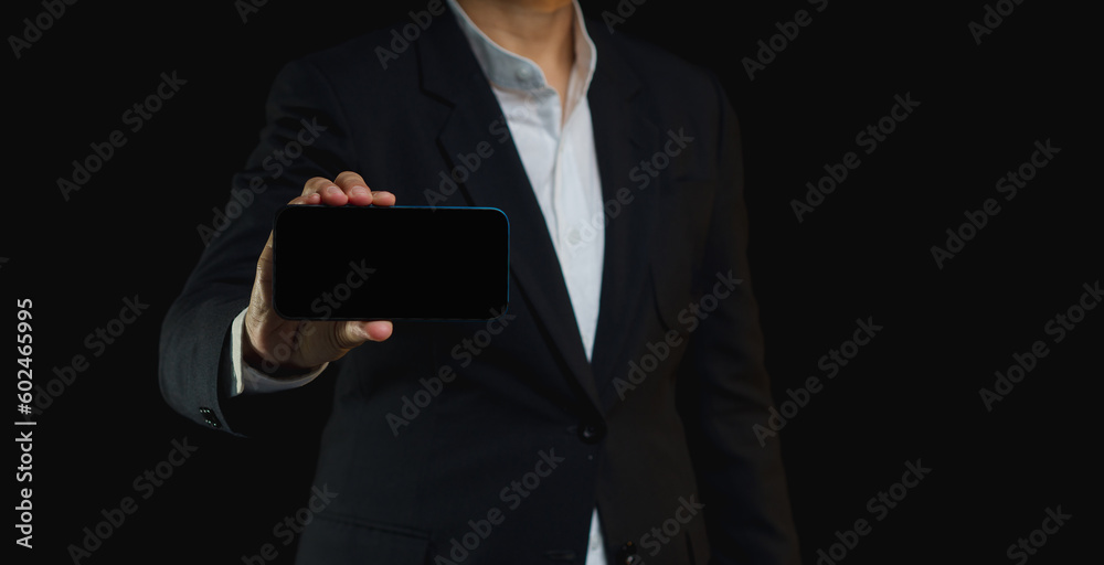 Businessman holding a blank screen smartphone horizontally against a black background.