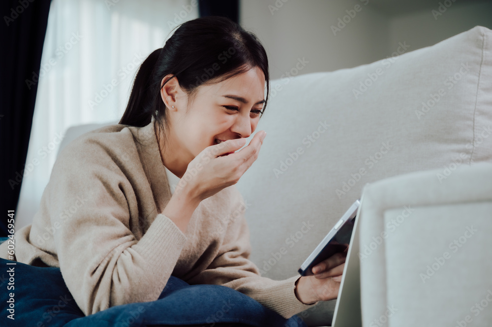 Happy young asian woman relax on comfortable couch at home texting messaging on smartphone, smiling girl use cellphone, browse wireless internet on gadget, shopping online from home Happy young asian woman relax on comfortable couch at home texting messaging on smartphone, smiling girl use cellphone, browse wireless internet on gadget, shopping online from home