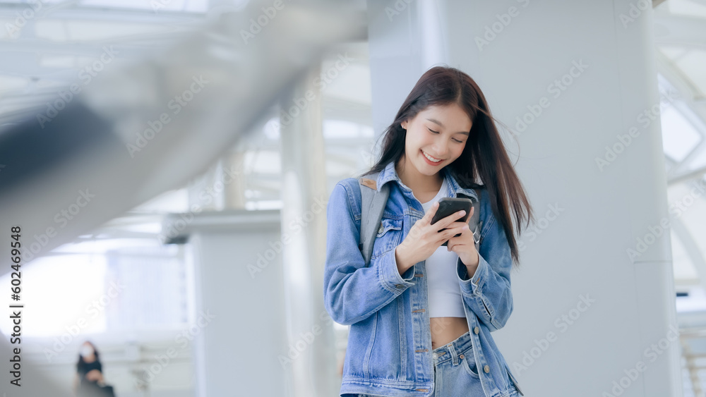 Young asian woman smiling using mobile smart phone outdoor. Happy female tourist wearing jeans jacket and holding smartphone at public Young asian woman smiling using mobile smart phone outdoor. Happy female tourist wearing jeans jacket and holding smartphone at public